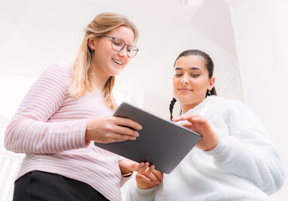 Lehrende blickt mit Schlerin auf ein Tablet